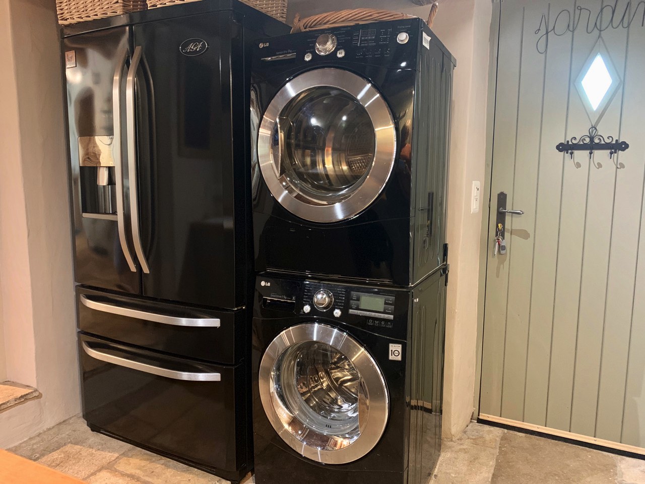 A modern kitchen with a stacked washer and dryer next to a stainless steel refrigerator, featuring a quaint wooden sign that reads 'jardin' on a rustic door.